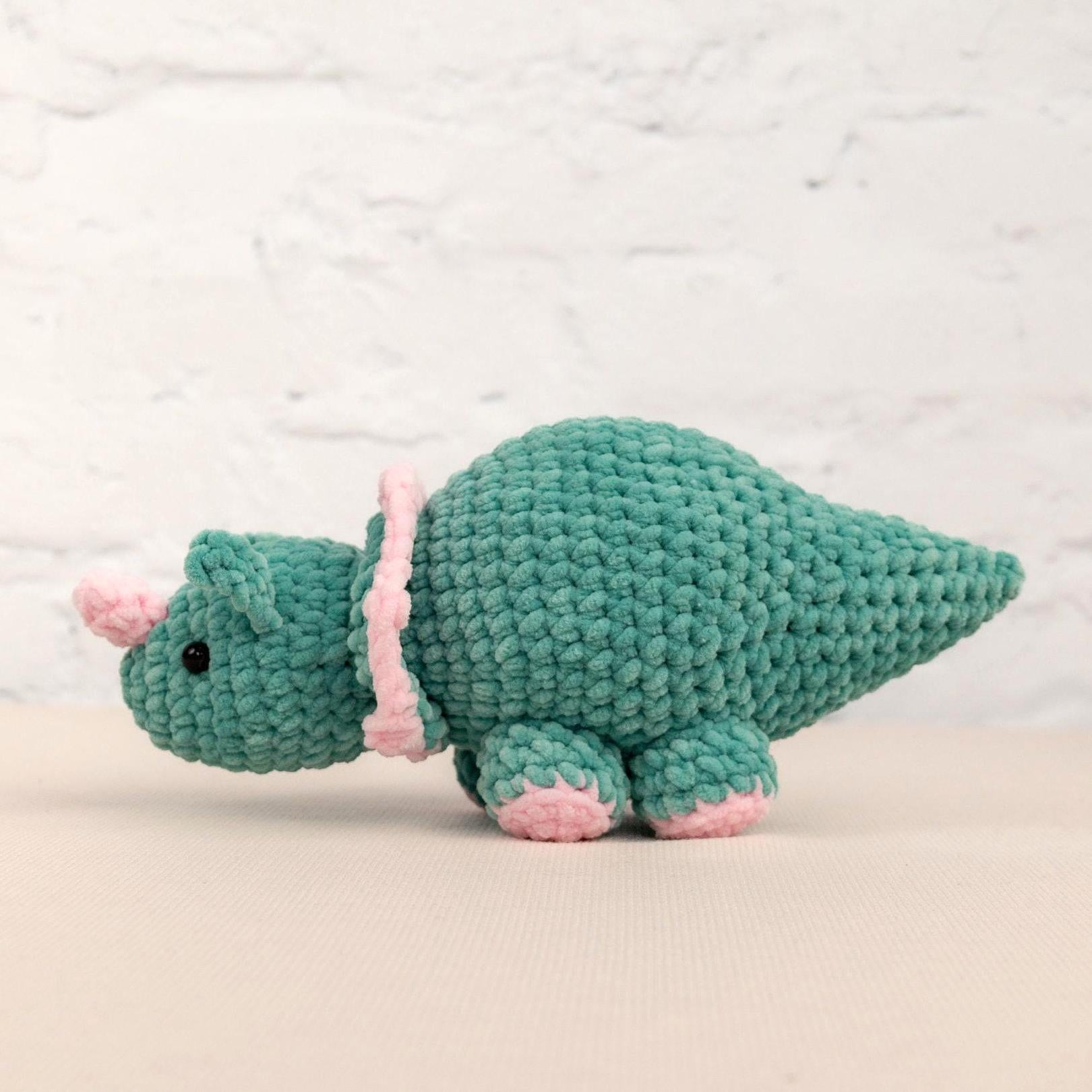 a crocheted green stuffed animal with a pink tail